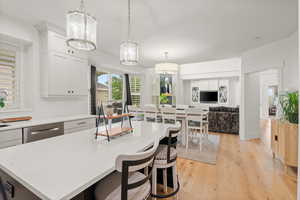 Kitchen featuring light countertops, light wood-style floors, pendant lighting, and white cabinets
