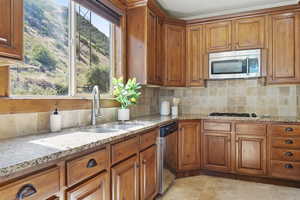 Kitchen featuring stainless steel appliances, brown cabinets, tasteful backsplash, and light stone countertops