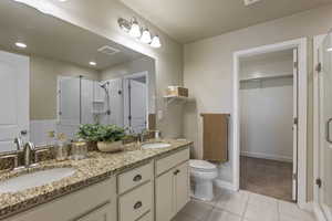 Bathroom with a shower stall, tile patterned floors, double vanity, and a walk in closet