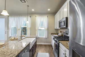 Kitchen with stainless steel appliances, wood finished floors, white cabinetry, decorative light fixtures, and recessed lighting