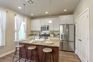Kitchen featuring stainless steel appliances, a breakfast bar area, white cabinetry, wood finished floors, and recessed lighting