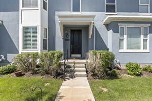 View of exterior entry with stucco siding and a yard