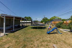 Fenced backyard featuring a trampoline, a playground, and a patio