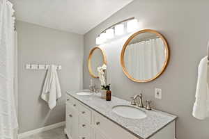 Bathroom with double vanity, tile patterned floors, a textured ceiling, and a shower with shower curtain