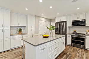 Kitchen with stainless steel appliances, white cabinetry, a kitchen breakfast bar, wood finished floors, and recessed lighting