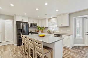 Kitchen featuring appliances with stainless steel finishes, white cabinets, light wood-style floors, a breakfast bar, and recessed lighting