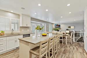 Kitchen with light wood finished floors, dishwasher, recessed lighting, a kitchen bar, and white cabinets