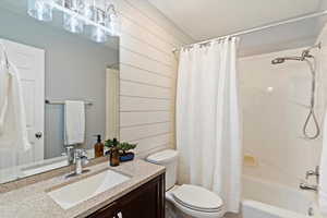 Bathroom with vanity, shower / bathtub combination with curtain, and wood walls