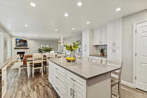 Kitchen with light wood finished floors, recessed lighting, a kitchen island, white cabinets, and a breakfast bar area