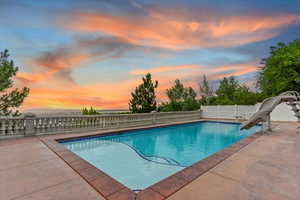 Pool at dusk featuring a water slide, a fenced backyard, and a patio area