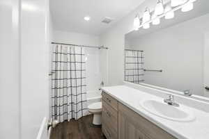Bathroom with vanity, wood finished floors, shower / bathtub combination with curtain, and recessed lighting