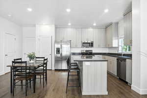 Kitchen with appliances with stainless steel finishes, a kitchen island, dark countertops, dark wood-style floors, and a breakfast bar