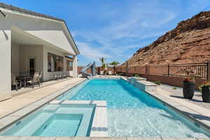 View of pool with a water slide, a fenced backyard, a patio area, a pool with connected hot tub, and a mountain view