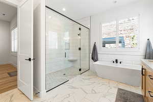 Bathroom featuring marble look tile flooring, a freestanding bath, a stall shower, recessed lighting, and vanity