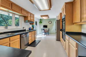 Kitchen featuring stainless steel appliances, dark countertops, finished concrete floors, and under cabinet range hood