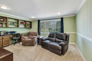 Office space with built in desk, crown molding, and light colored carpet