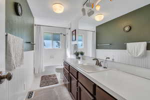 Full bathroom featuring vanity, shower / bathtub combination with curtain, a wainscoted wall, and tile patterned floors