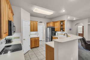 Kitchen featuring arched walkways, white electric range oven, freestanding refrigerator, light countertops, and a peninsula