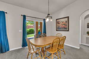 Dining space featuring arched walkways, carpet flooring, and vaulted ceiling