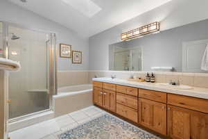 Full bathroom featuring a skylight, lofted ceiling, a stall shower, tile patterned floors, and double vanity