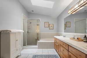Bathroom with a bath, a stall shower, tile patterned floors, a skylight, and double vanity