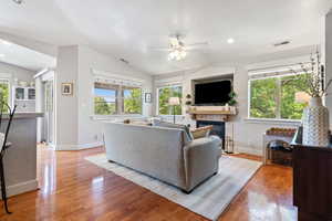 Living room featuring vaulted ceiling, a ceiling fan, healthy amount of natural light, a tiled fireplace, and light wood-style floors