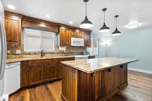 Kitchen featuring white appliances, tasteful backsplash, dark wood-type flooring, a center island, and hanging light fixtures