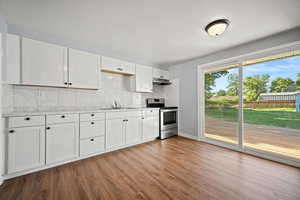 Kitchen with electric range, under cabinet range hood, wood finished floors, and decorative backsplash