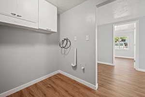 Laundry room with cabinet space, hookup for a washing machine, light wood finished floors, a textured ceiling, and hookup for a gas dryer