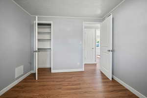 Unfurnished bedroom featuring ornamental molding, wood finished floors, a closet, and a textured ceiling