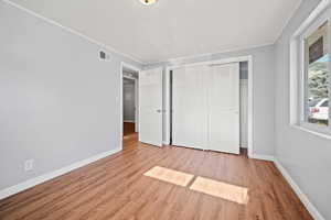 Unfurnished bedroom with wood finished floors, crown molding, and a closet