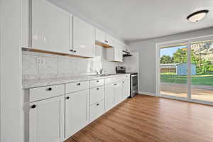 Kitchen with stainless steel electric range oven, under cabinet range hood, light countertops, light wood-style floors, and backsplash