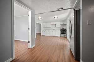 Kitchen featuring stainless steel appliances, wood finished floors, white cabinetry, under cabinet range hood, and light countertops