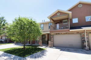 Multi unit property featuring stucco siding, stone siding, a garage, a balcony, and concrete driveway