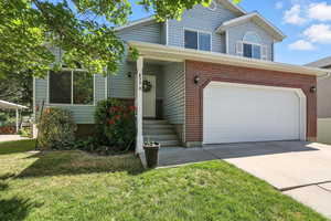 View of front of property featuring brick siding, concrete driveway, a front lawn, and a garage