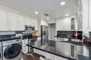 Kitchen with stainless steel appliances, washing machine and dryer, a breakfast bar area, a peninsula, and glass insert cabinets