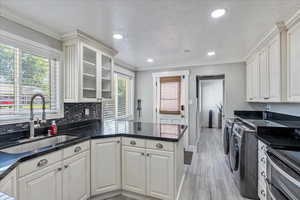 Kitchen featuring separate washer and dryer, a peninsula, light wood-type flooring, white cabinets, and ornamental molding