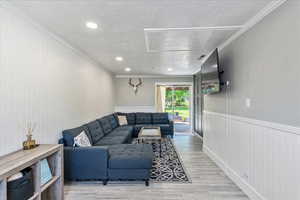Living area featuring a textured ceiling, crown molding, a wainscoted wall, light wood-style flooring, and recessed lighting