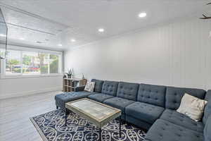 Living area with wood finished floors, recessed lighting, crown molding, a textured ceiling, and attic access