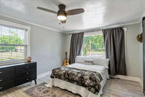 Bedroom featuring multiple windows, a textured ceiling, light wood-style floors, crown molding, and a ceiling fan