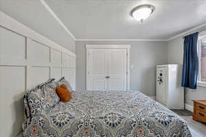 Bedroom with crown molding, wood finished floors, a textured ceiling, multiple windows, and a closet