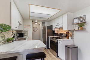 Kitchen with appliances with stainless steel finishes, under cabinet range hood, backsplash, light wood finished floors, and white cabinets