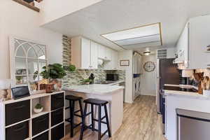 Kitchen with washer and dryer, black microwave, light countertops, a peninsula, and decorative backsplash