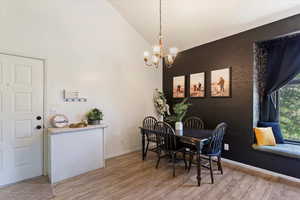 Dining area with a chandelier, light wood finished floors, and high vaulted ceiling