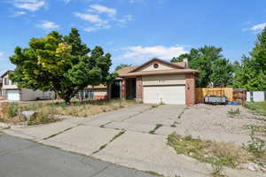 View of front of home featuring brick siding, an attached garage, driveway, a chimney, and a gate
