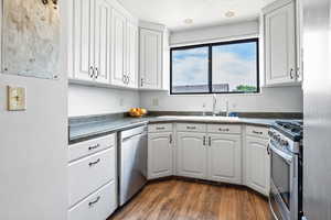 Kitchen with stainless steel appliances, dark countertops, white cabinetry, and dark wood-type flooring