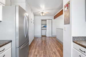 Kitchen featuring freestanding refrigerator, dark countertops, white cabinets, ceiling fan, and dark wood finished floors