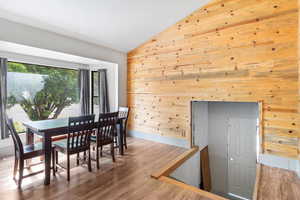 Dining area featuring vaulted ceiling, wooden walls, and wood finished floors