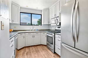 Kitchen with stainless steel appliances, dark countertops, white cabinetry, light wood finished floors, and a textured ceiling