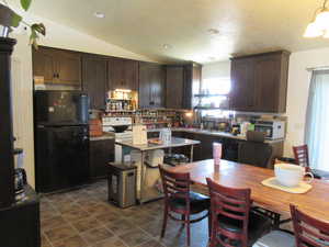 Kitchen with freestanding refrigerator, range, dark brown cabinetry, and vaulted ceiling